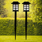 A pair of sleek black solar garden lights illuminating a lush green lawn at dusk.